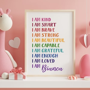 Op de afbeelding: Een ingelijst print met regenboogkleurige tekst die "Ik ben aardig, ik ben slim, ik ben dapper, ik ben sterk, ik ben mooi, ik ben bekwaam, ik ben dankbaar, ik ben genoeg, ik ben geliefd, ik ben Bianca" zegt.