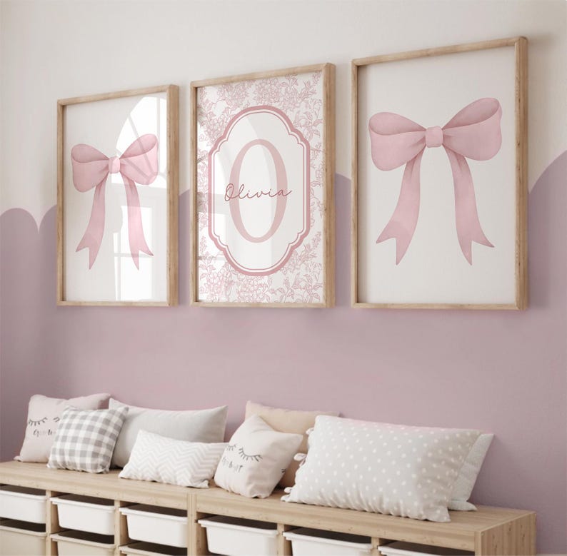 Puede incluir: Tres impresiones art&iacute;sticas enmarcadas con un acabado de madera clara. Dos impresiones presentan una ilustraci&oacute;n de lazo rosa, mientras que la impresi&oacute;n central muestra el nombre "Olivia" en cursiva dentro de un marco floral rosa. Las impresiones se exhiben sobre un banco de madera.