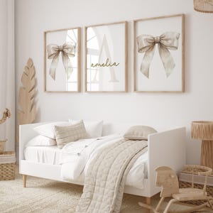 May include: Three framed prints featuring a watercolour bow design in beige and brown tones. The middle print features the name "amelia" in gold lettering.