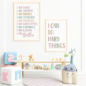 Pu&ograve; includere: Due stampe incorniciate con testo motivazionale in una cameretta per bambini. La prima stampa dice "Sono gentile, sono intelligente, sono coraggioso, sono forte, sono abbastanza, sono grato, sono capace, sono amato, sono Bella". La seconda stampa dice "Posso fare cose difficili".