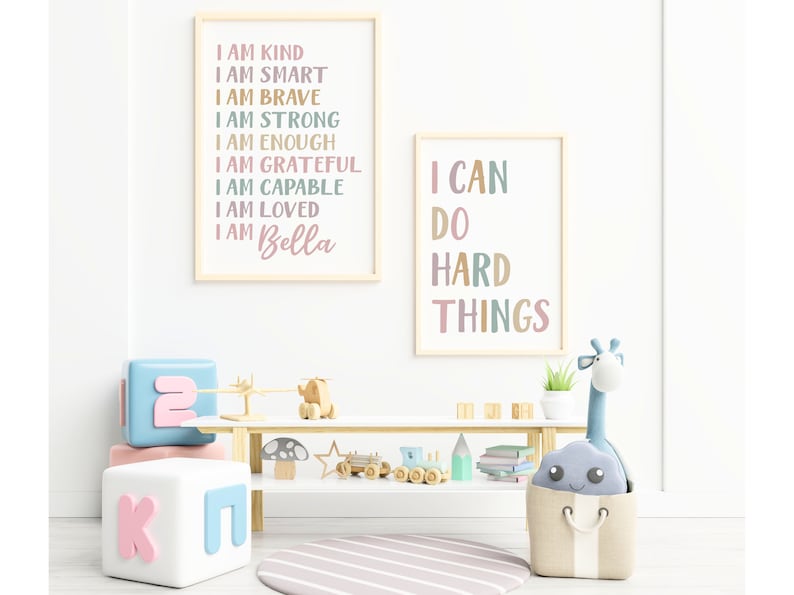 Pu&ograve; includere: Due stampe incorniciate con testo motivazionale in una cameretta per bambini. La prima stampa dice "Sono gentile, sono intelligente, sono coraggioso, sono forte, sono abbastanza, sono grato, sono capace, sono amato, sono Bella". La seconda stampa dice "Posso fare cose difficili".