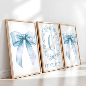 May include: Three framed prints with a light blue watercolor bow, a light blue watercolor letter C with a decorative frame, and the name Charlotte in a light blue font.
