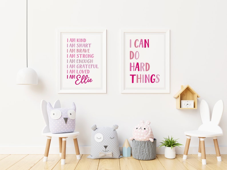 Pu&ograve; includere: Due stampe incorniciate con testo rosa e bianco su sfondo bianco. La stampa a sinistra recita "Sono gentile, sono intelligente, sono coraggioso, sono forte, sono abbastanza, sono grato, sono amato, sono Ellie". La stampa a destra recita "Posso fare cose difficili".