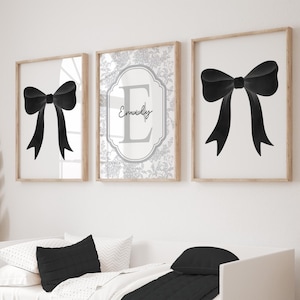 Puede incluir: Tres obras de arte enmarcadas. Dos presentan un lazo negro sobre fondo blanco. La tercera tiene un dise&ntilde;o floral con el nombre "Emily" y la letra "E". Los marcos son de color madera clara.