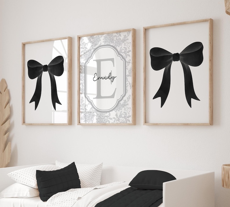 Puede incluir: Tres obras de arte enmarcadas. Dos presentan un lazo negro sobre fondo blanco. La tercera tiene un dise&ntilde;o floral con el nombre "Emily" y la letra "E". Los marcos son de color madera clara.