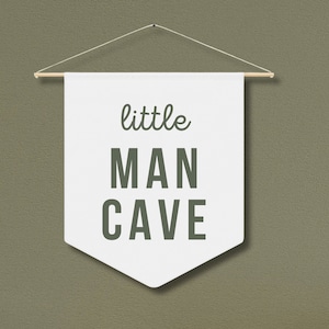 Peut inclure: Banni&egrave;re blanche avec le texte "little MAN CAVE" en lettres vertes, suspendue &agrave; une baguette en bois.