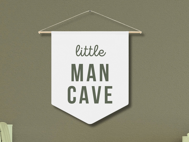 Peut inclure: Banni&egrave;re blanche avec le texte "little MAN CAVE" en lettres vertes, suspendue &agrave; une baguette en bois.