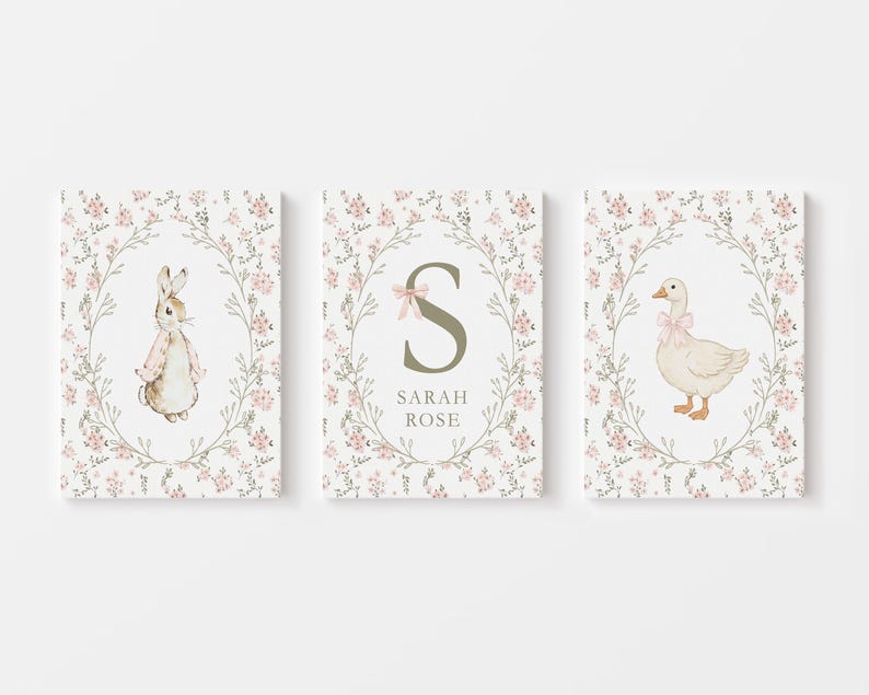May include: Three framed art prints featuring a bunny, a goose, and the letter "S" with the name "SARAH ROSE". Each print has a floral wreath border with pink flowers and green leaves. The bunny and goose wear pink bows.