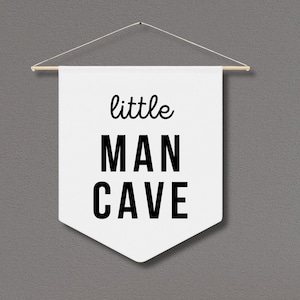 Peut inclure: Banni&egrave;re blanche avec du texte noir qui dit "little MAN CAVE" suspendue &agrave; une baguette en bois.