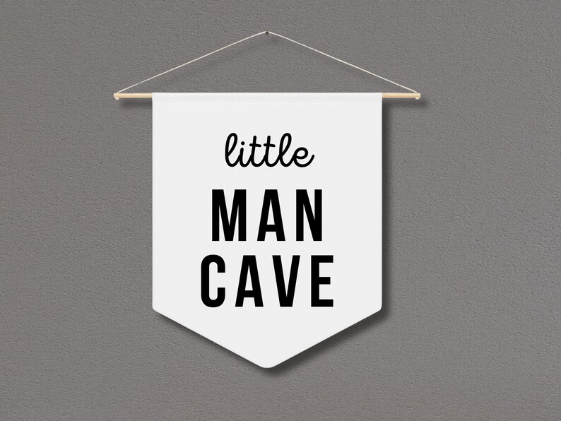 Peut inclure: Banni&egrave;re blanche avec du texte noir qui dit "little MAN CAVE" suspendue &agrave; une baguette en bois.