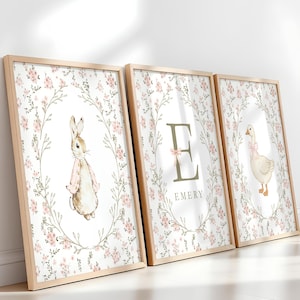 May include: Three framed prints with a floral wreath design. One features a rabbit, another a letter "E" with the name "Emery", and the third a goose. The prints have a light wood frame and a soft, watercolor style.