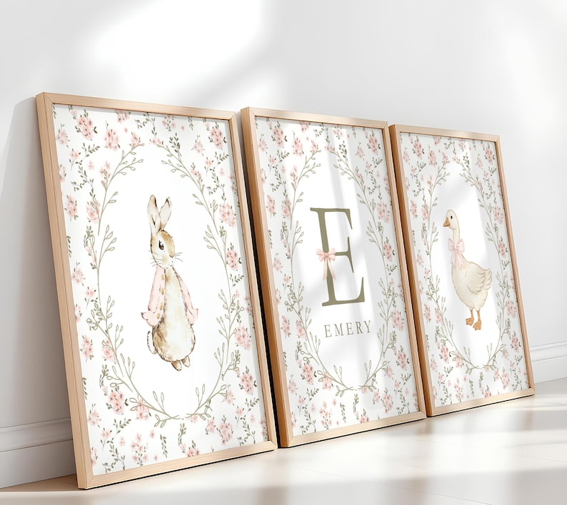 May include: Three framed prints with a floral wreath design. One features a rabbit, another a letter "E" with the name "Emery", and the third a goose. The prints have a light wood frame and a soft, watercolor style.