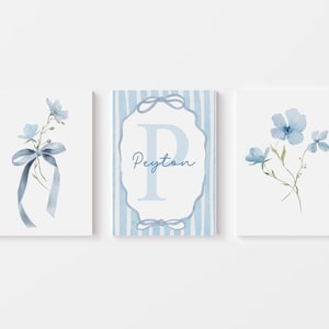 May include: Three framed watercolor prints featuring blue floral designs. One print displays a bouquet with a ribbon, another has a floral arrangement, and the third showcases a monogram with the name "Peyton". The prints have a soft, pastel color palette.