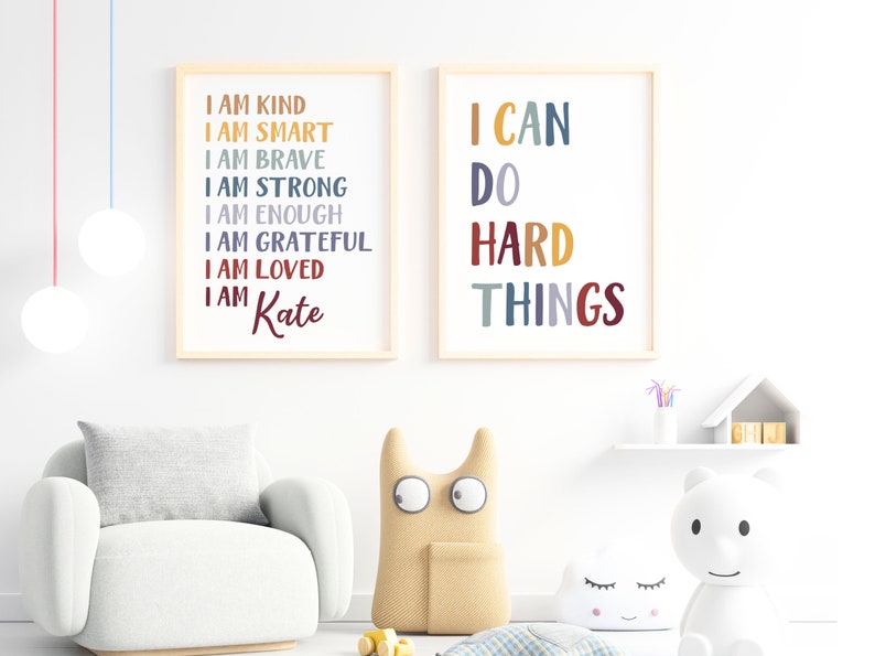 Pu&ograve; includere: Due stampe incorniciate con testo motivazionale in una camera da letto per bambini. La prima stampa dice "Sono gentile, sono intelligente, sono coraggioso, sono forte, sono abbastanza, sono grato, sono amato, sono Kate". La seconda stampa dice "Posso fare cose difficili".