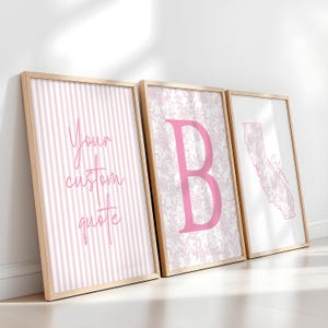 May include: Three framed wall art prints in light wood frames. The first print features pink vertical stripes and the text Your custom quote. The second print displays a large pink letter B over a floral pattern. The third shows a map of California.