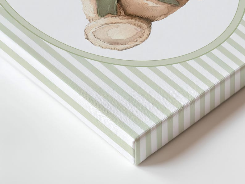 May include: A canvas print featuring a watercolour illustration of a teddy bear with a green bow. The canvas edges are wrapped with a light green and white striped pattern, creating a soft, vintage aesthetic.