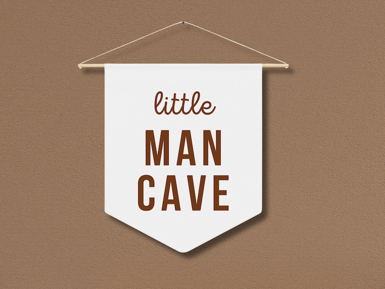 Peut inclure: Banni&egrave;re blanche avec du texte brun qui dit "little MAN CAVE" accroch&eacute;e &agrave; un mur brun.