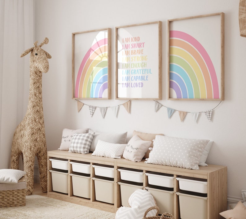 May include: Three framed rainbow prints with positive affirmations, including "I am kind", "I am smart", "I am brave", "I am strong", "I am enough", "I am grateful", "I am capable", and "I am loved". The prints are hung on a white wall above a wooden storage bench with white bins.