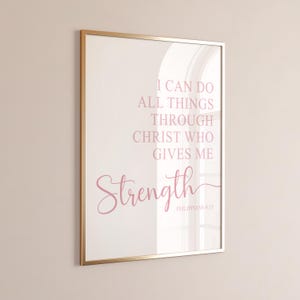 May include: A framed print with a gold-colored frame. The print features the text "I CAN DO ALL THINGS THROUGH CHRIST WHO GIVES ME Strength" in a soft pink color. The text is from Philippians 4:13.