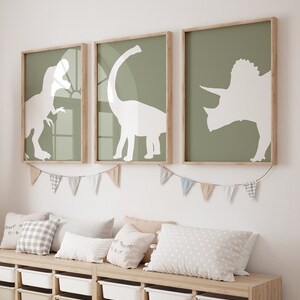 May include: Three framed prints of white dinosaur silhouettes on a green background. The prints are hung on a white wall above a wooden bench with pillows.