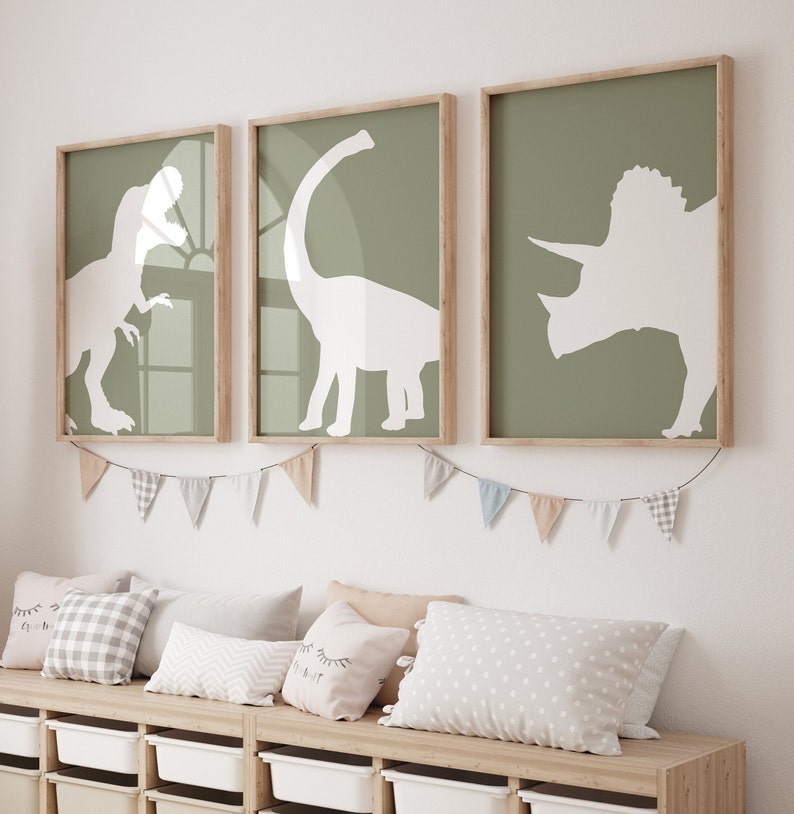 May include: Three framed prints of white dinosaur silhouettes on a green background. The prints are hung on a white wall above a wooden bench with pillows.