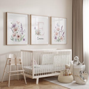 May include: Three framed floral art prints with watercolor flowers in pink, purple, and green hues. The middle print features the letter "E" and the name "Emma". A white crib, high chair, and decorative baskets complete the nursery scene.