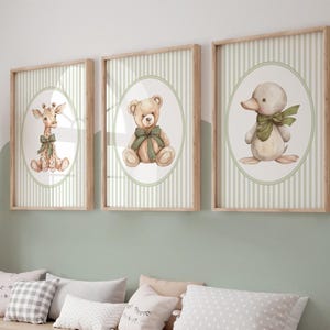 May include: Three framed nursery art prints. Each print features a different animal: a giraffe, a teddy bear, and a duckling, all with green bows. The illustrations are set in oval frames against a green and white striped background, with light wood frames.