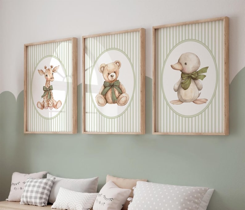 May include: Three framed nursery art prints. Each print features a different animal: a giraffe, a teddy bear, and a duckling, all with green bows. The illustrations are set in oval frames against a green and white striped background, with light wood frames.