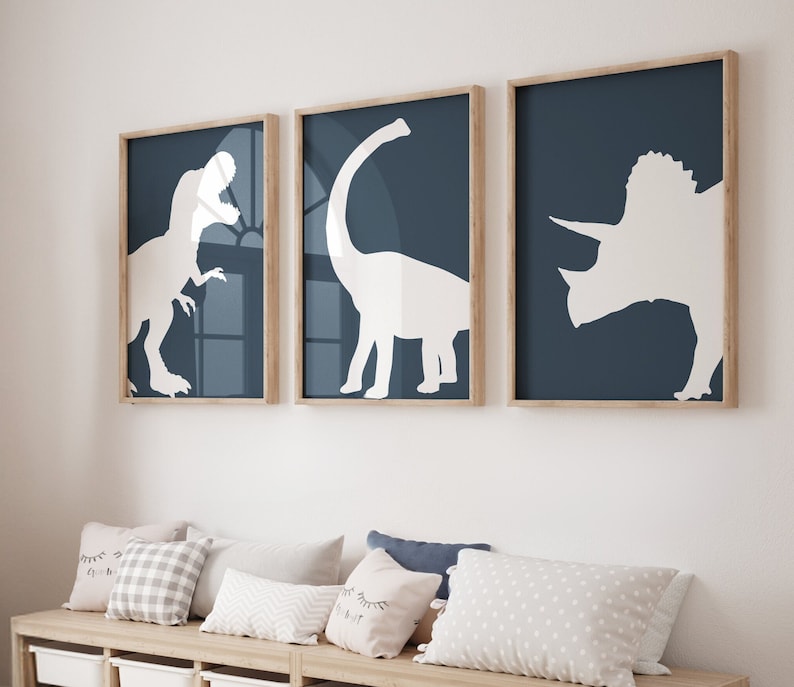 May include: Three framed prints with blue backgrounds and white silhouettes of dinosaurs. The prints feature a Tyrannosaurus Rex, a Brachiosaurus, and a Triceratops.