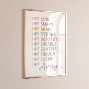 May include: A framed wall art print featuring the text I AM KIND, I AM SMART, I AM BRAVE, I AM STRONG, I AM BEAUTIFUL, I AM CAPABLE, I AM GRATEFUL, I AM ENOUGH, I AM LOVED, and I AM Avery in various pastel colors including pink, yellow, and teal.