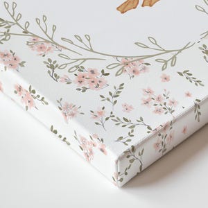 May include: Close-up of a canvas print featuring a floral design. The print has a white background with a pattern of pink flowers and green leaves. The edges of the canvas are also printed with the floral pattern.