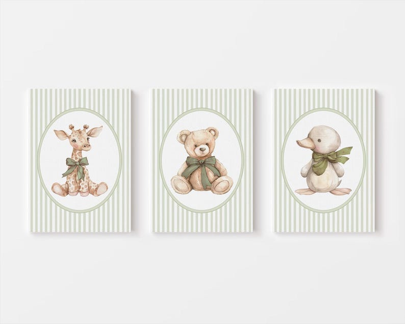 May include: Three framed art prints with watercolour illustrations of a giraffe, teddy bear, and duck. Each animal has a green bow and is set against a striped background. The frames are rectangular with an oval border.