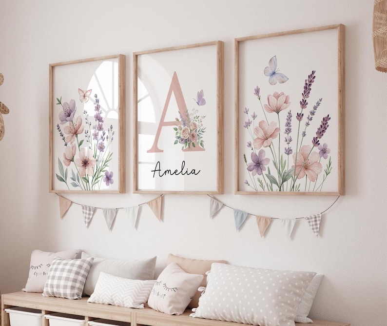 May include: Three framed floral art prints with watercolor illustrations of flowers and butterflies in soft pink, purple, and green hues. One print features the letter "A" and the name "Amelia". The frames are light wood.