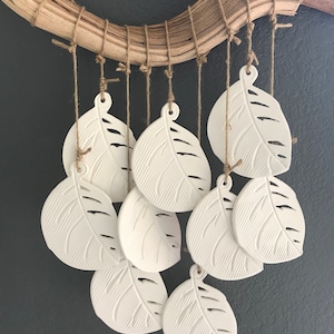 May include: A white ceramic wind chime with leaf-shaped pendants hanging from a driftwood branch. The leaves are detailed with a textured pattern and are suspended from twine.