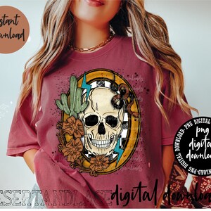 May include: A red t-shirt with a graphic design of a skull with a snake wrapped around it. The skull is surrounded by a yellow circle with a checkered pattern. There are flowers and a cactus on either side of the skull. The text "digital downloads" is at the bottom of the image.