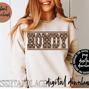 Puede incluir: Una sudadera beige con la palabra "HOWDY" impresa en letras a cuadros marrones y negras. Las letras tienen un aspecto desgastado y vintage.