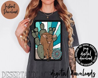 May include: A dark gray t-shirt with a graphic design of a brown calf standing in a desert landscape with cacti and a turquoise sunburst. The text "png digital download" is in a circle on the bottom right corner of the image.