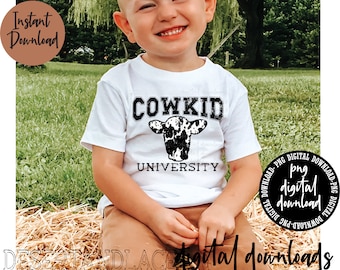 May include: A young child wearing a white t-shirt with a black and white cow graphic and the text "COWKID UNIVERSITY".