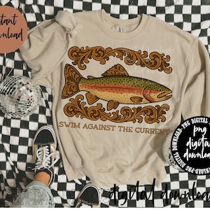 May include: Beige sweatshirt featuring a detailed illustration of a rainbow trout with ornate, brown scrollwork. The text "SWIM AGAINST THE CURRENT" is below the fish. The words "Instant Download" and "digital download" are also visible.