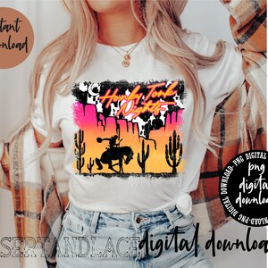 May include: A white t-shirt with a graphic design of a cowboy riding a horse in front of a sunset. The graphic also includes the text "Honky Tonk Nights" in pink and black lettering.