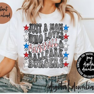 May include: A white t-shirt with a distressed gray graphic that says "Just a Mom Who Loves Baseball & Ballpark Burgers". The graphic is decorated with red, white, and blue stars.