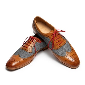 May include: A pair of brown leather shoes with gray tweed accents and red laces. The shoes have a wingtip design and are a classic style.