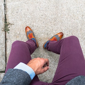 May include: A person wearing a gray blazer, a white and blue striped shirt, burgundy pants, and brown and blue patterned shoes with red laces.