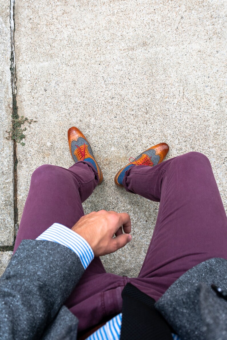 May include: A person wearing a gray blazer, a white and blue striped shirt, burgundy pants, and brown and blue patterned shoes with red laces.