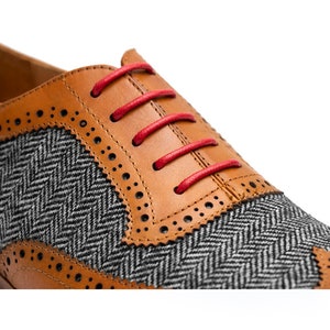 May include: Close-up of a brown leather oxford shoe with a gray and black herringbone pattern on the toe. The shoe has red laces.