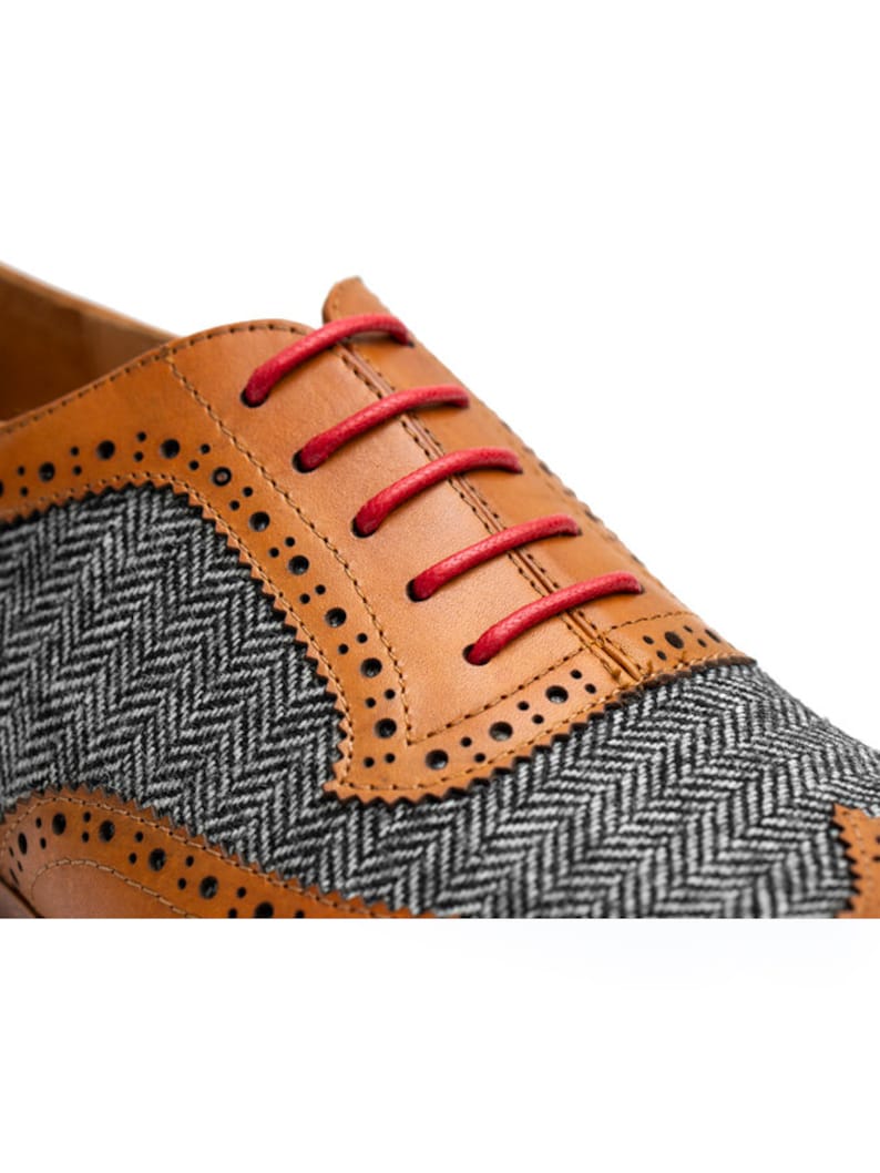 May include: Close-up of a brown leather oxford shoe with a gray and black herringbone pattern on the toe. The shoe has red laces.
