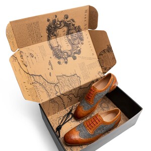 May include: A pair of brown leather shoes with grey tweed accents and red laces in a box with a vintage map design.