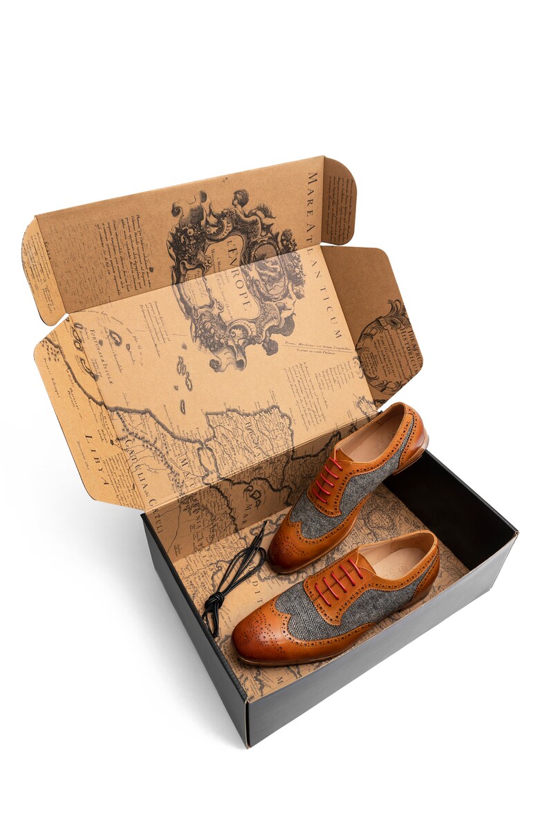 May include: A pair of brown leather shoes with grey tweed accents and red laces in a box with a vintage map design.