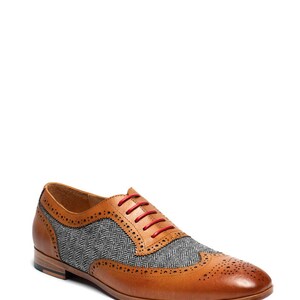 May include: Tan leather brogue shoes with a gray and black tweed pattern on the toe and side panels. The shoes have red laces.