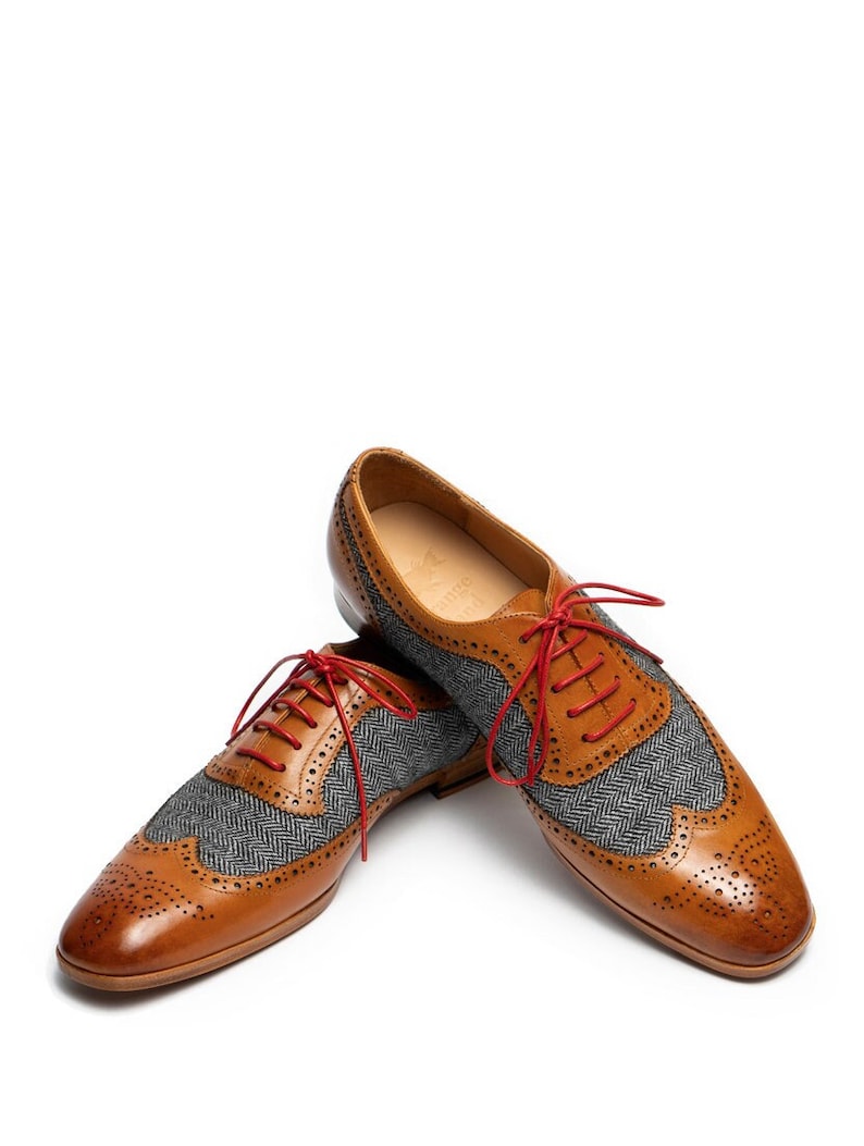 May include: A pair of brown leather shoes with gray tweed accents and red laces. The shoes have a wingtip design and are a classic style.